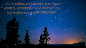 Immagine che cattura le prime luci dell'alba tra un cielo stellato, accompagnata da un augurio per un martedì luminoso e sereno