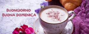 Immagine di una tazza di caffè accanto a fiori colorati su un tavolo, con la scritta 'Buongiorno e Buona Domenica'. Un breve pensiero di augurio per una giornata rilassante e positiv
